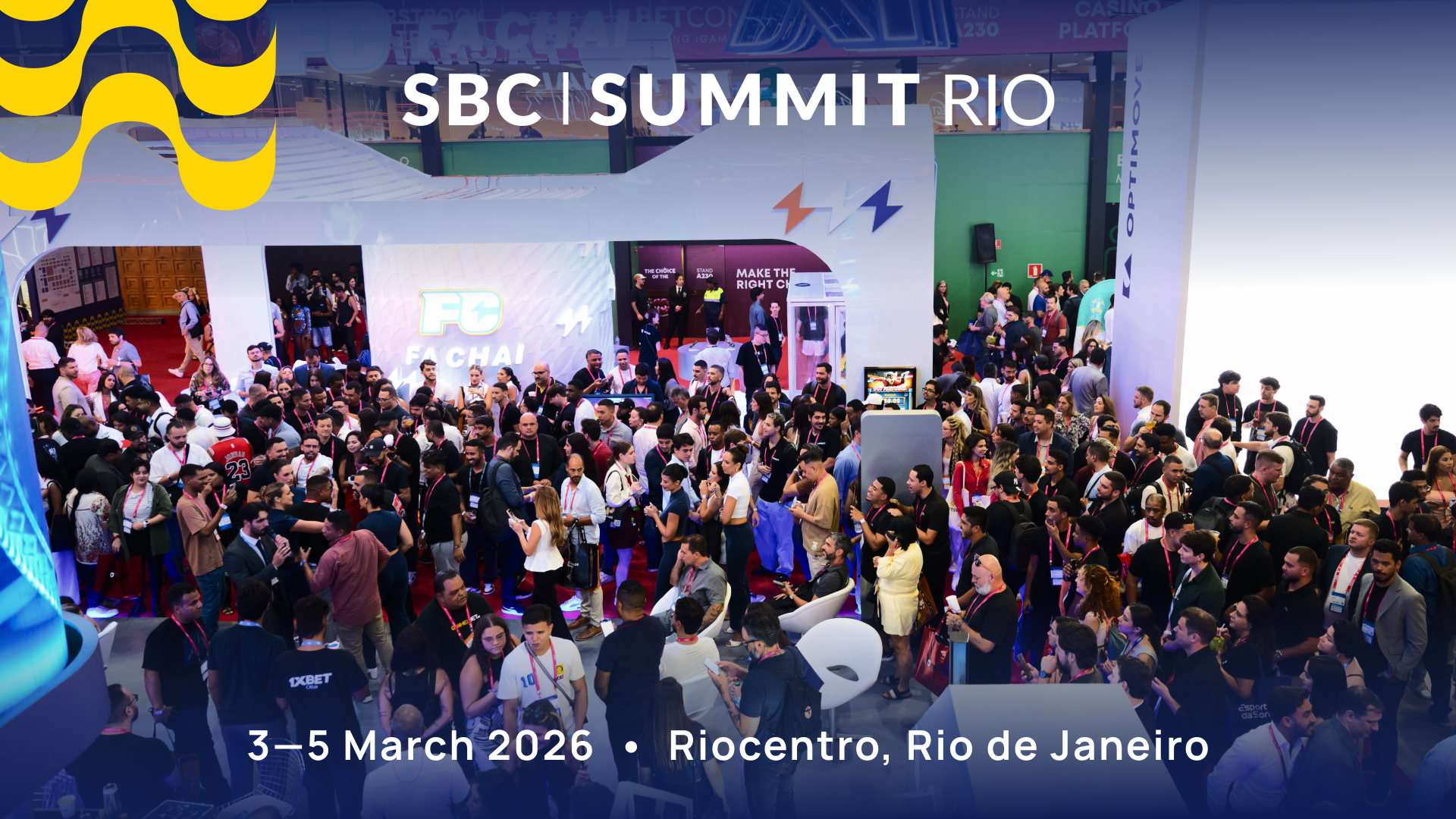 Attendees networking and walking across the busy exhibition floor at SBC Summit Rio 2026 at Riocentro, with industry booths and betting and gaming professionals meeting and discussing business.